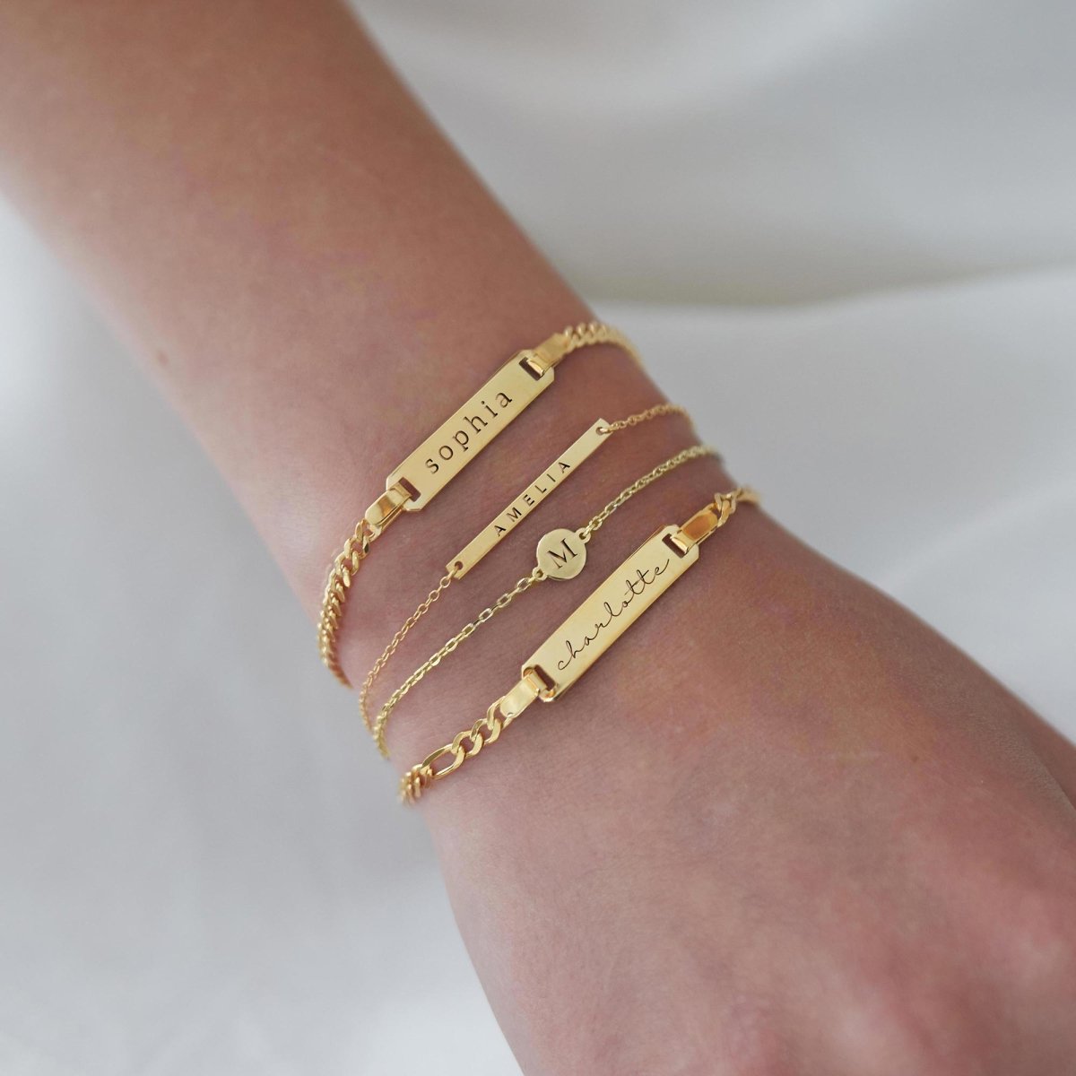 14K gold disc bracelet engraved with an initial, shown stacked with ID bracelets on a wrist