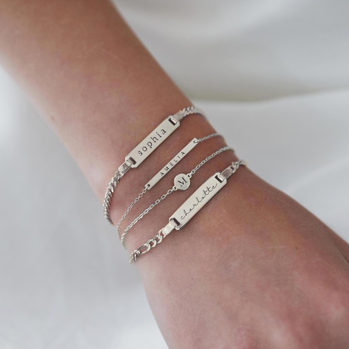 Sterling silver ID and bar bracelets, each engraved with a name, stacked on a model's wrist