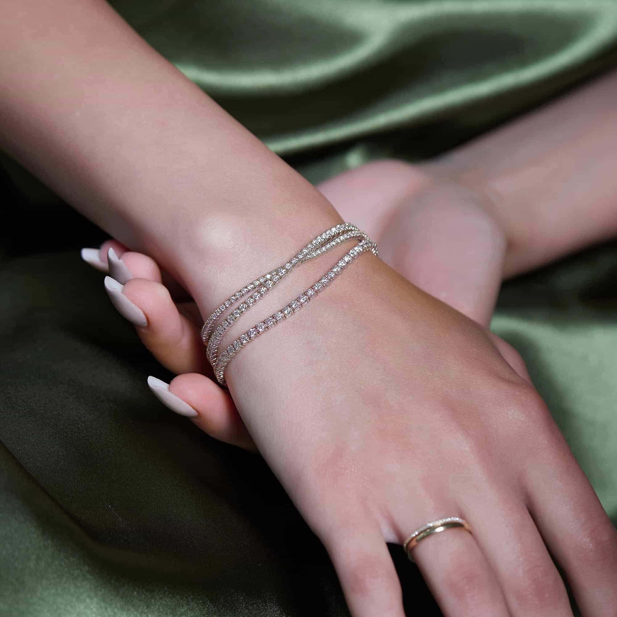 14K white gold diamond tennis bracelets stacked on a model's wrist over green satin