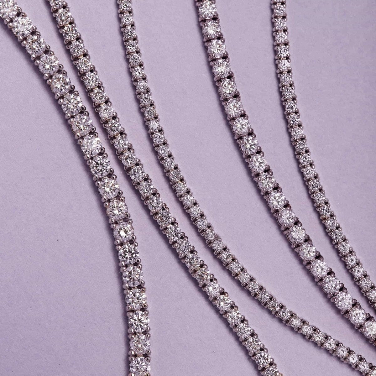 14K white gold diamond tennis bracelets in graduated widths, laid on lilac