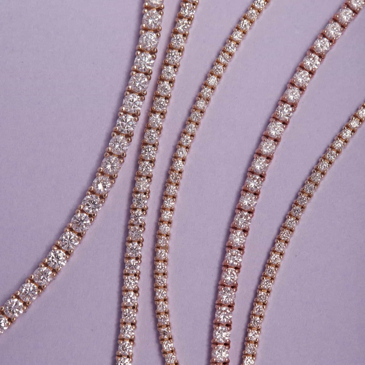 14K gold diamond tennis bracelets in graduated widths, laid on lilac