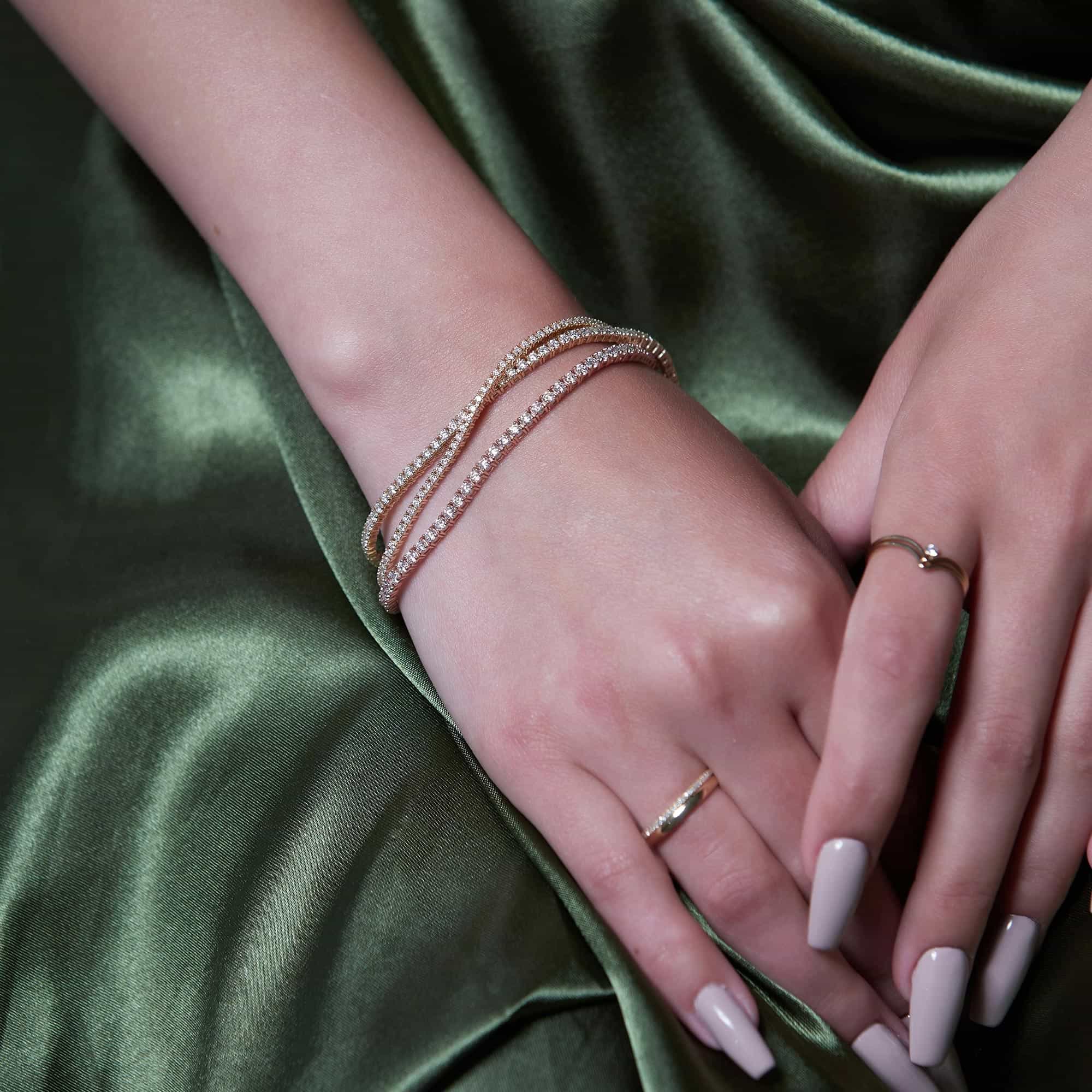 14K gold diamond tennis bracelets stacked on a model's wrist over green satin