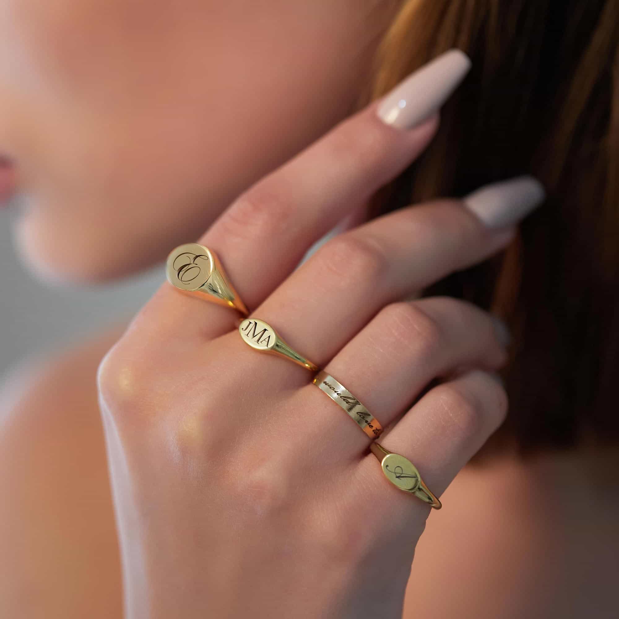 Gold vermeil oval signet rings engraved with initials, shown stacked on a model's hand