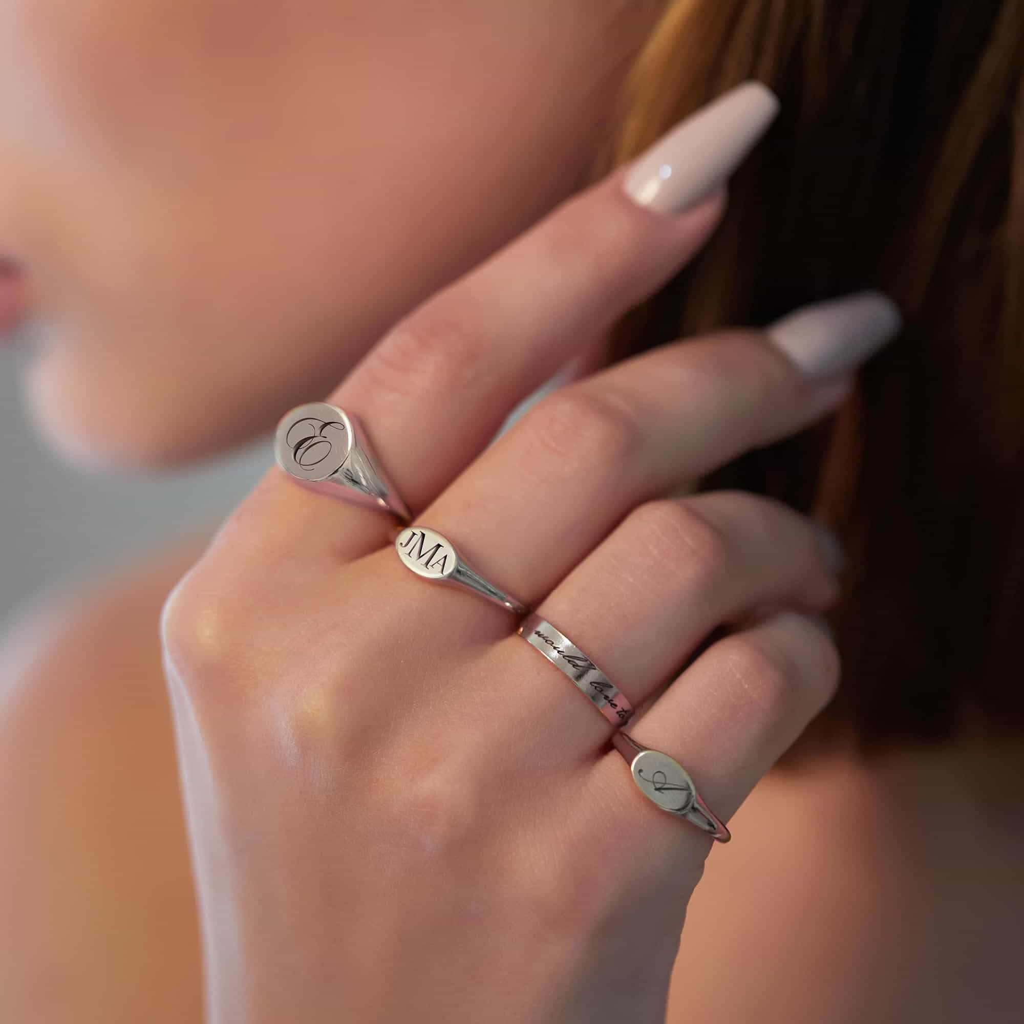 Sterling silver oval signet rings engraved with initials, shown stacked on a model's hand
