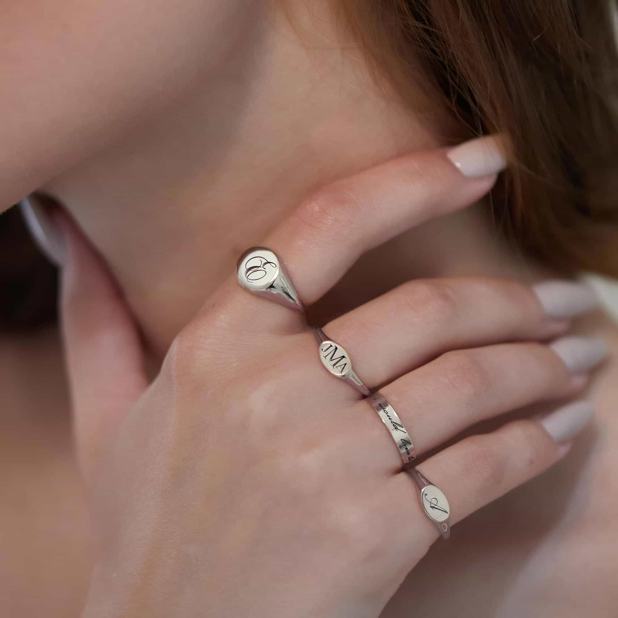 Sterling silver oval signet ring engraved with an initial, shown on a model's hand at the cheek