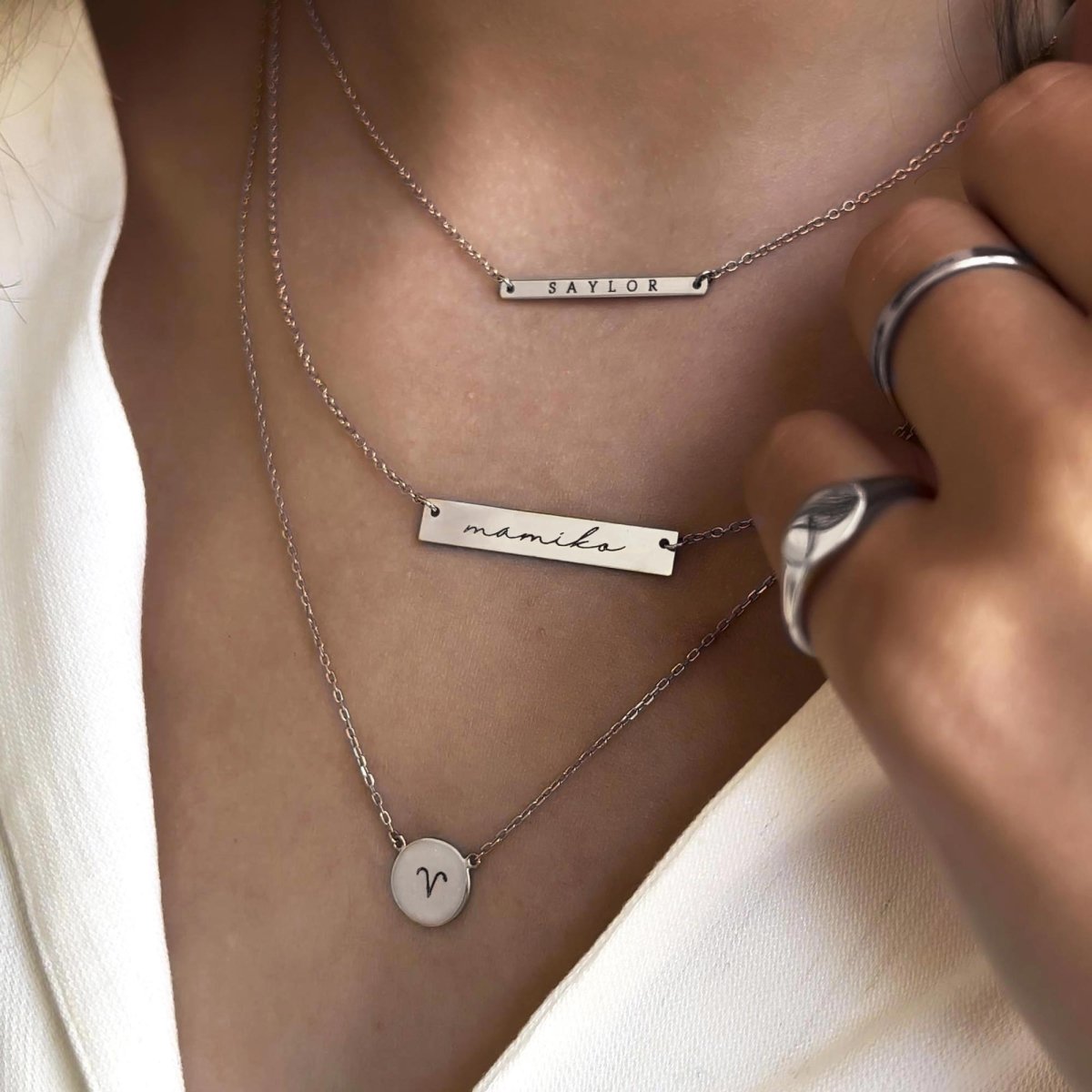 Sterling silver bar and disc necklaces engraved with names and an initial, layered on a model's neckline
