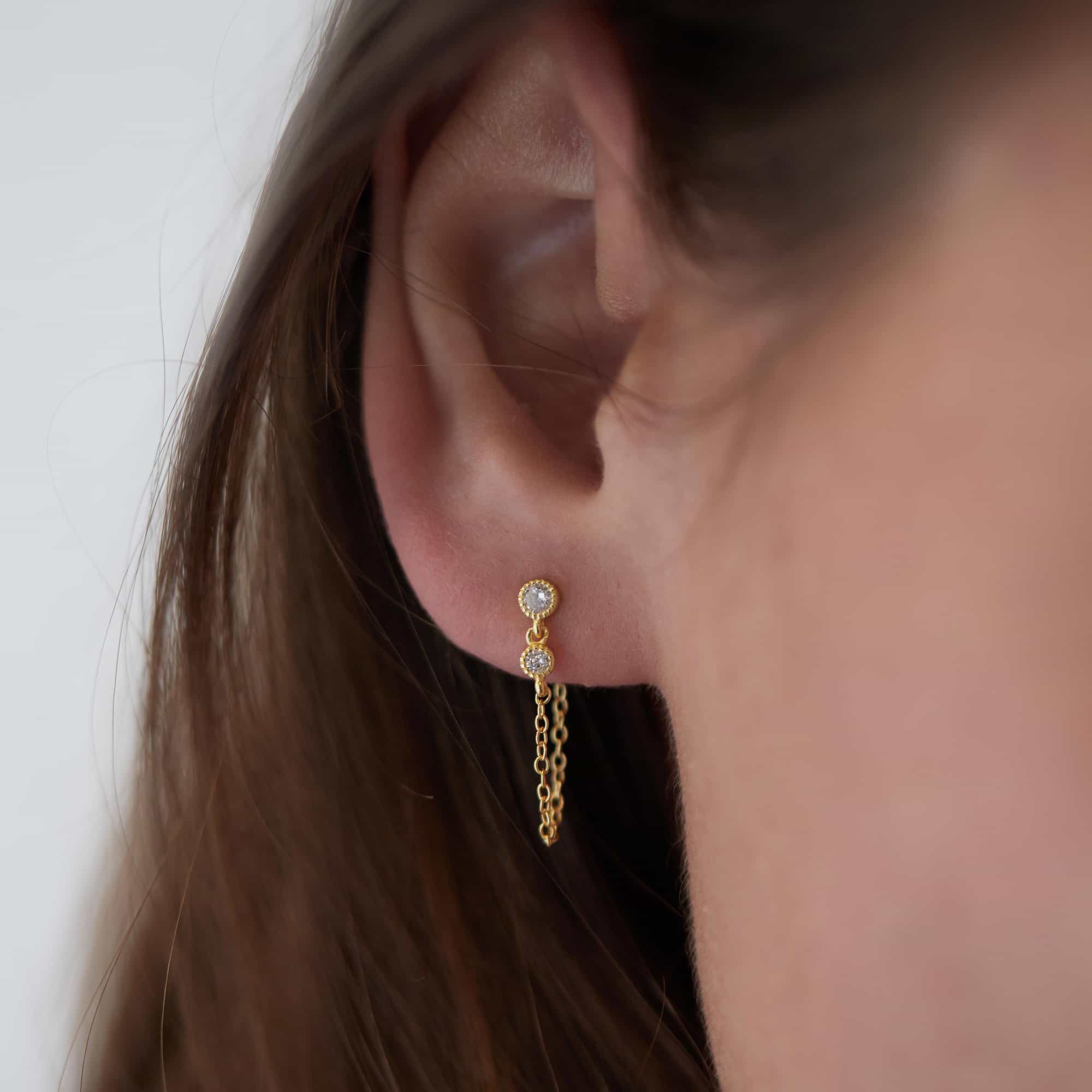 Gold vermeil double bezel chain earring with two white zirconia studs and a draped chain, on a model's ear
