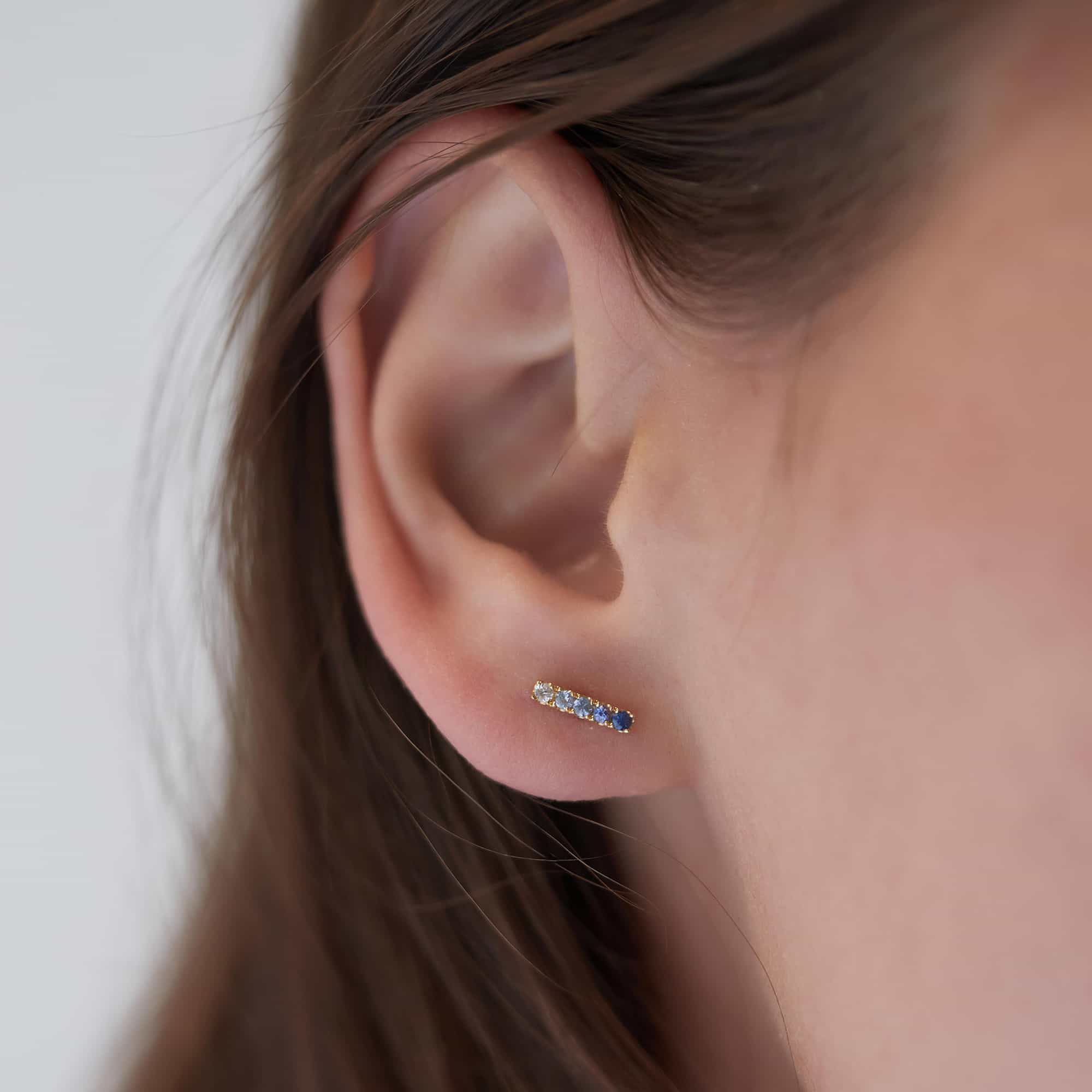 14K gold bar stud with ombre blue sapphire stones, shown on a model's lobe