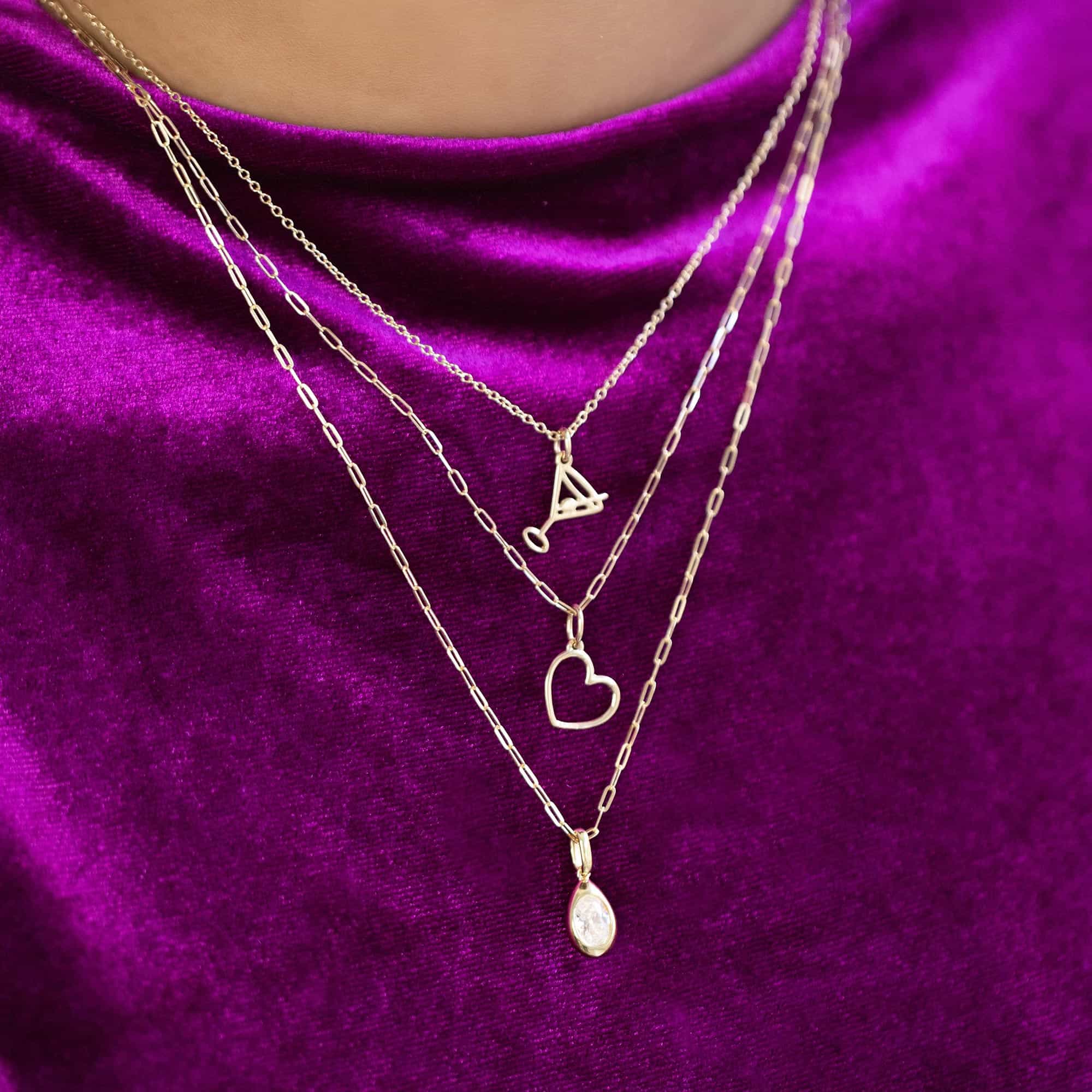 Layered gold necklaces with letter, heart and oval clear-stone pendants, on magenta velvet