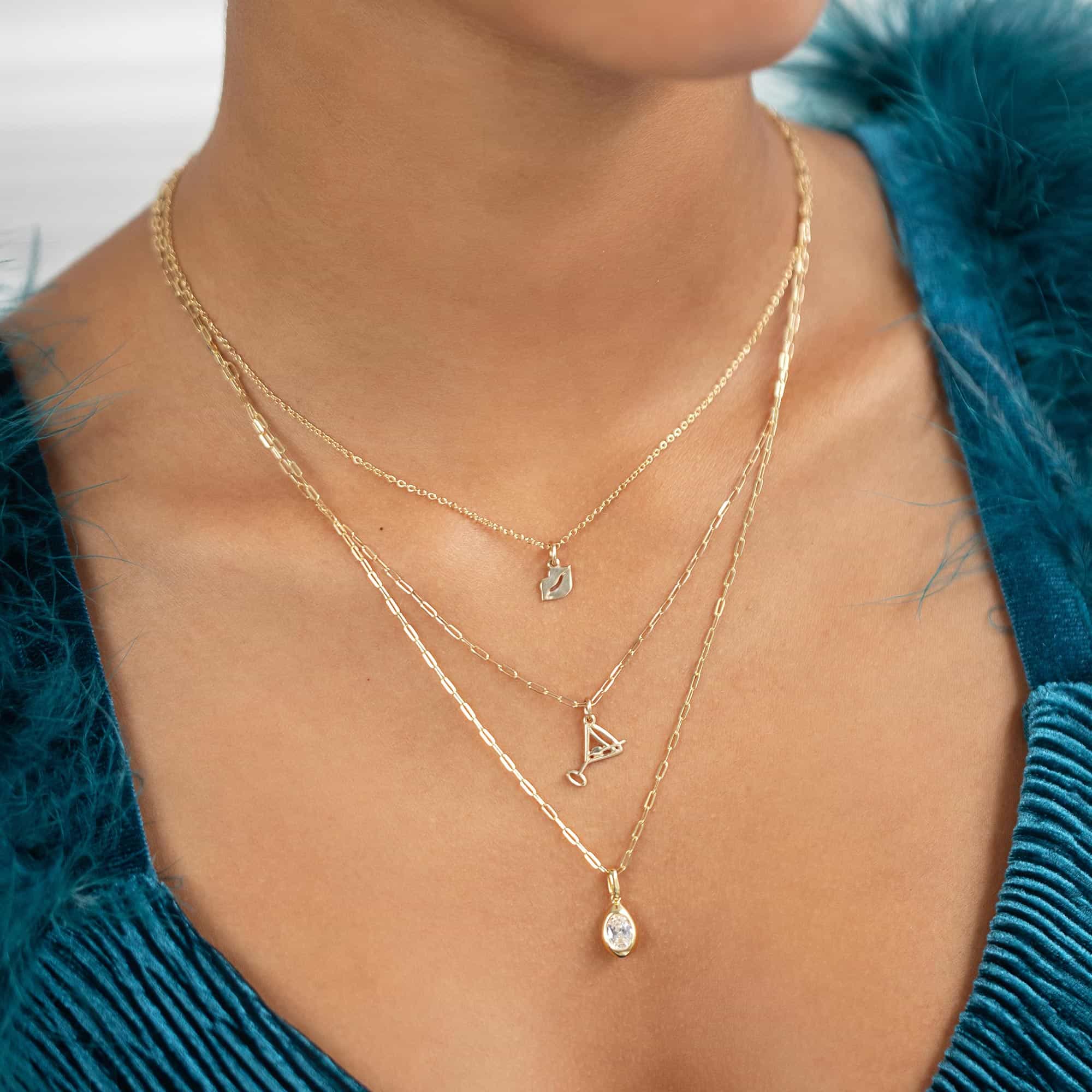 Layered gold necklaces with lip, martini-glass and oval clear-stone pendants, on a model's neckline