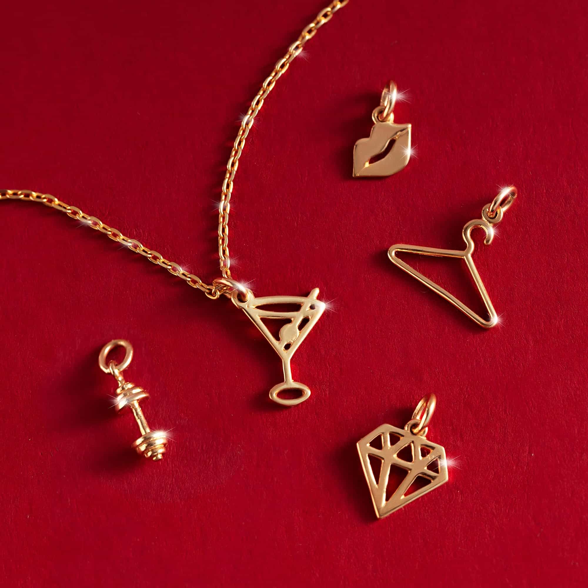 Gold charms including a clothes hanger, martini, lips, dumbbell and diamond shape, on a red background