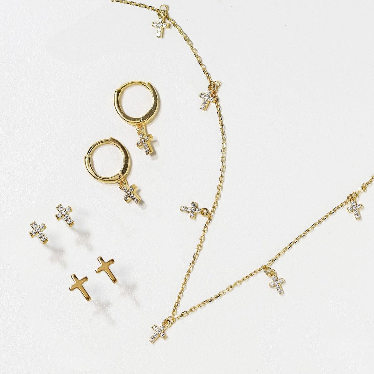 Gold cross studs, huggie hoops and chains laid out together on a white background