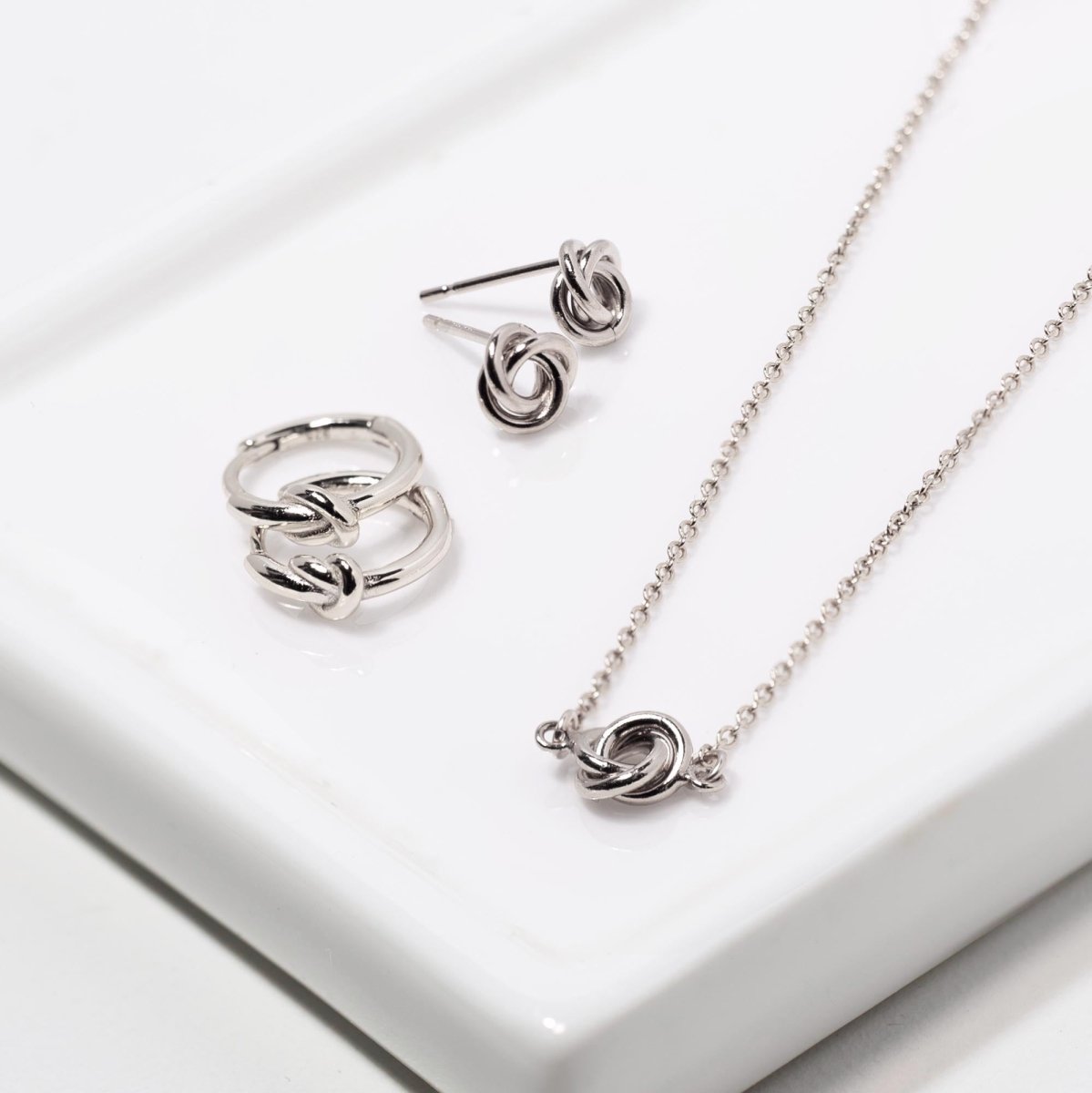 Sterling silver mini knot studs with matching knot huggies and necklace on a white tray
