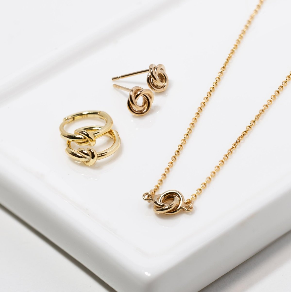 Gold vermeil knot huggie hoops with matching knot studs and a knot necklace on a white tray