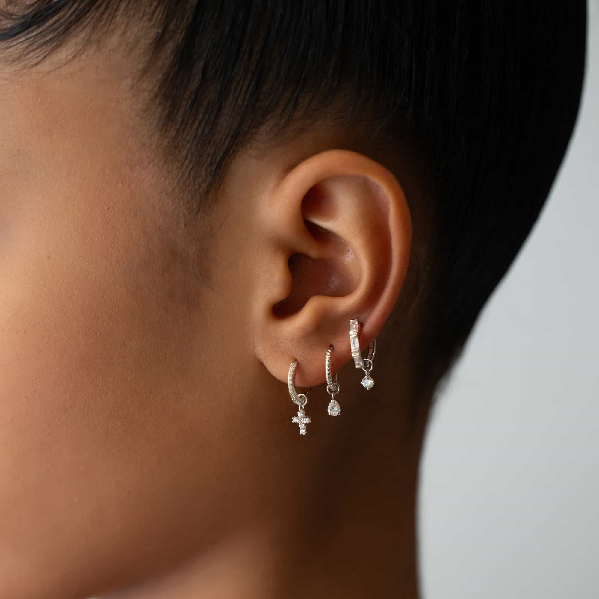 Close-up of woman's ear featuring White Gold Texture Rope Huggie Hoop Earrings paired with Moissanite Tear Pear Gemstone and 14K White Gold Single Thin Pave Huggie Moissanite Crystals.