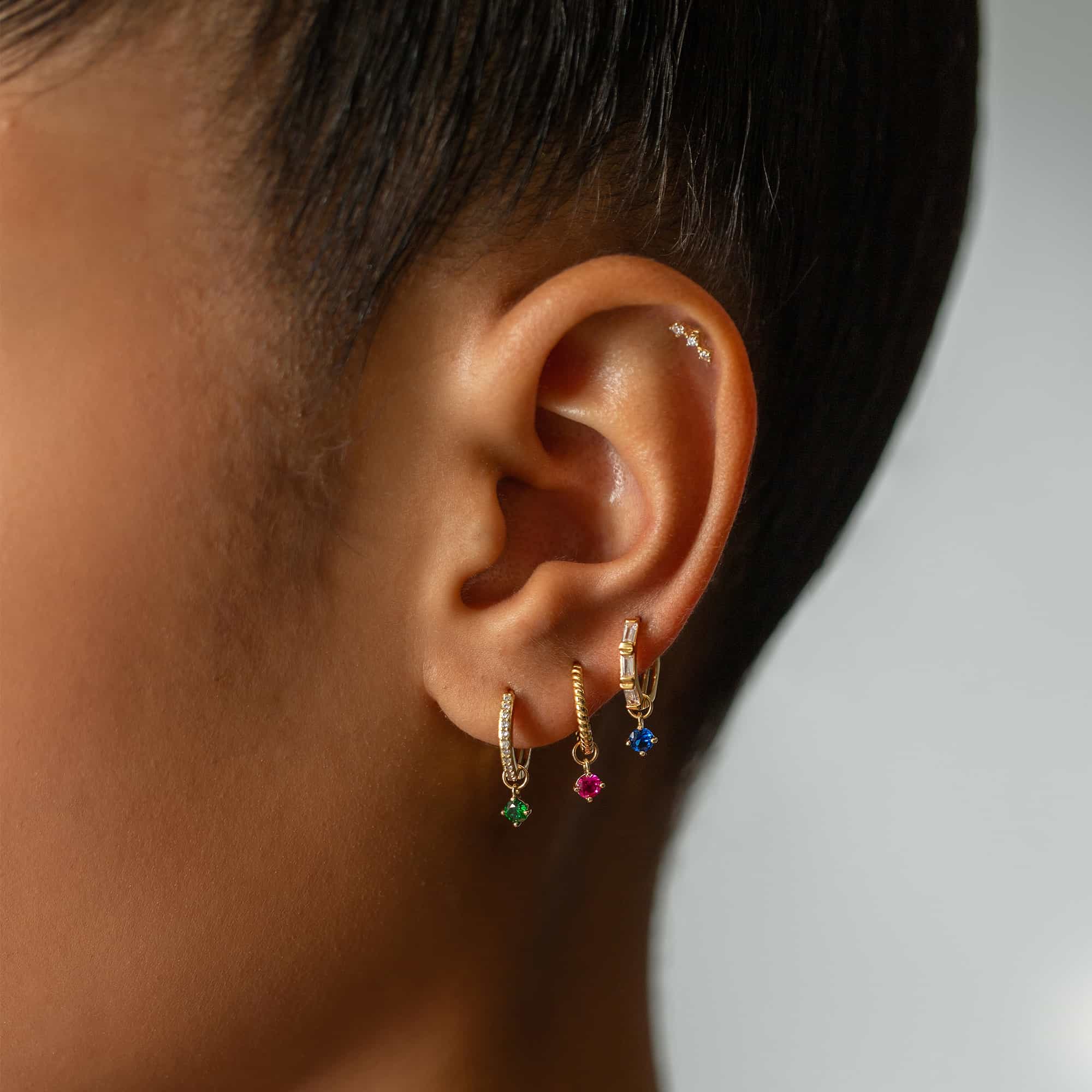 14K gold pavé huggie hoops with green, pink and blue stone charms shown on a model's ear