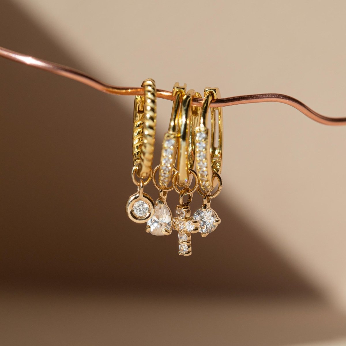 14K gold crystal cross charm shown beside colorful round and teardrop birthstone charms, on a cream background