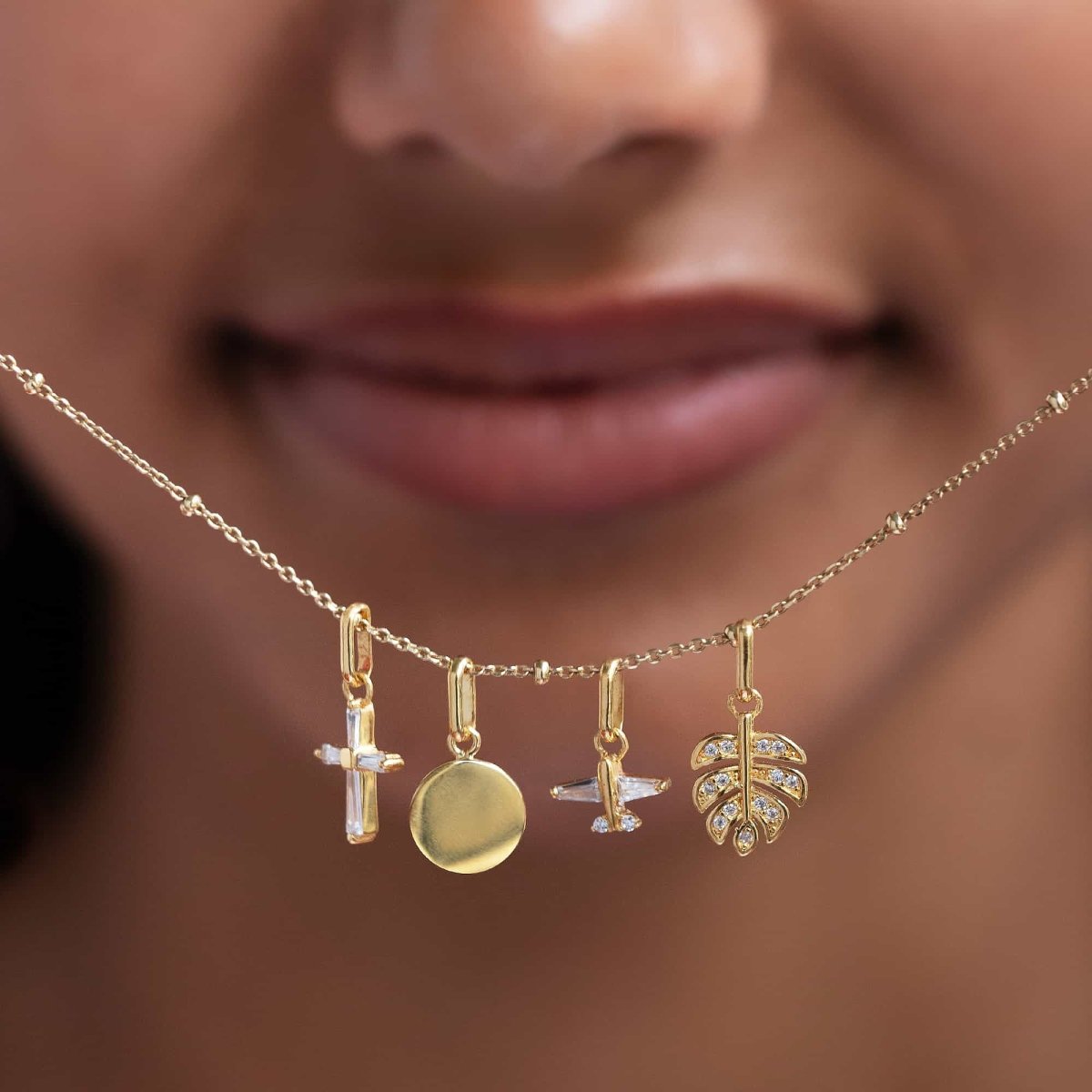 Gold cross charm with clear baguette stones shown with other charms on a chain, on a model's neckline