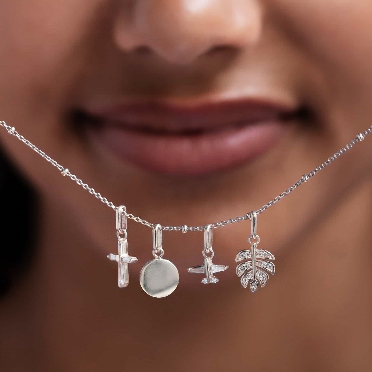 Sterling silver airplane, disc and leaf charms with clear stones on a beaded chain, shown on a neckline