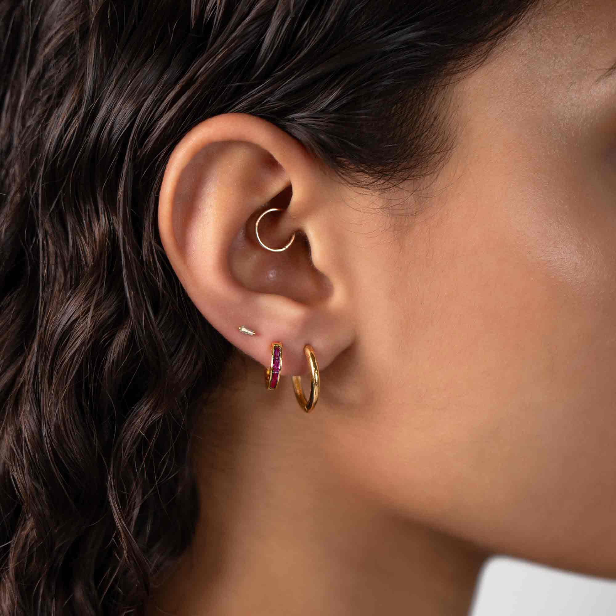 Gold vermeil baguette ruby huggie hoop with red stones, shown on a model's lobe next to a plain hoop