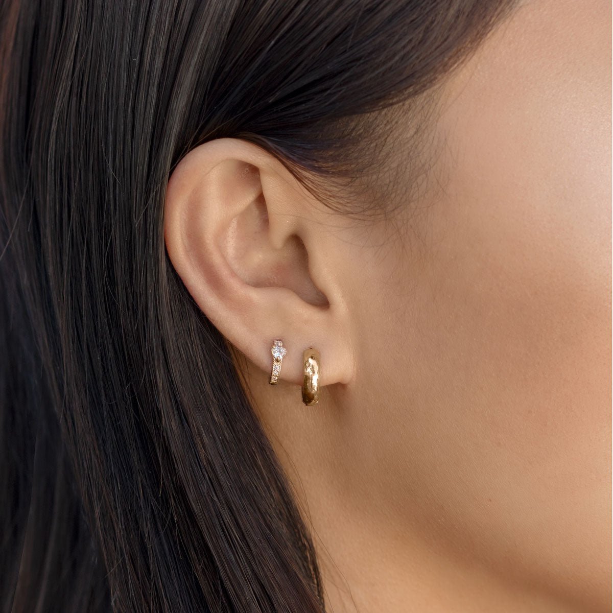 Close up of woman's ear featuring Gold Vermeil Tiny Heart Huggies paired with gold huggie earring 