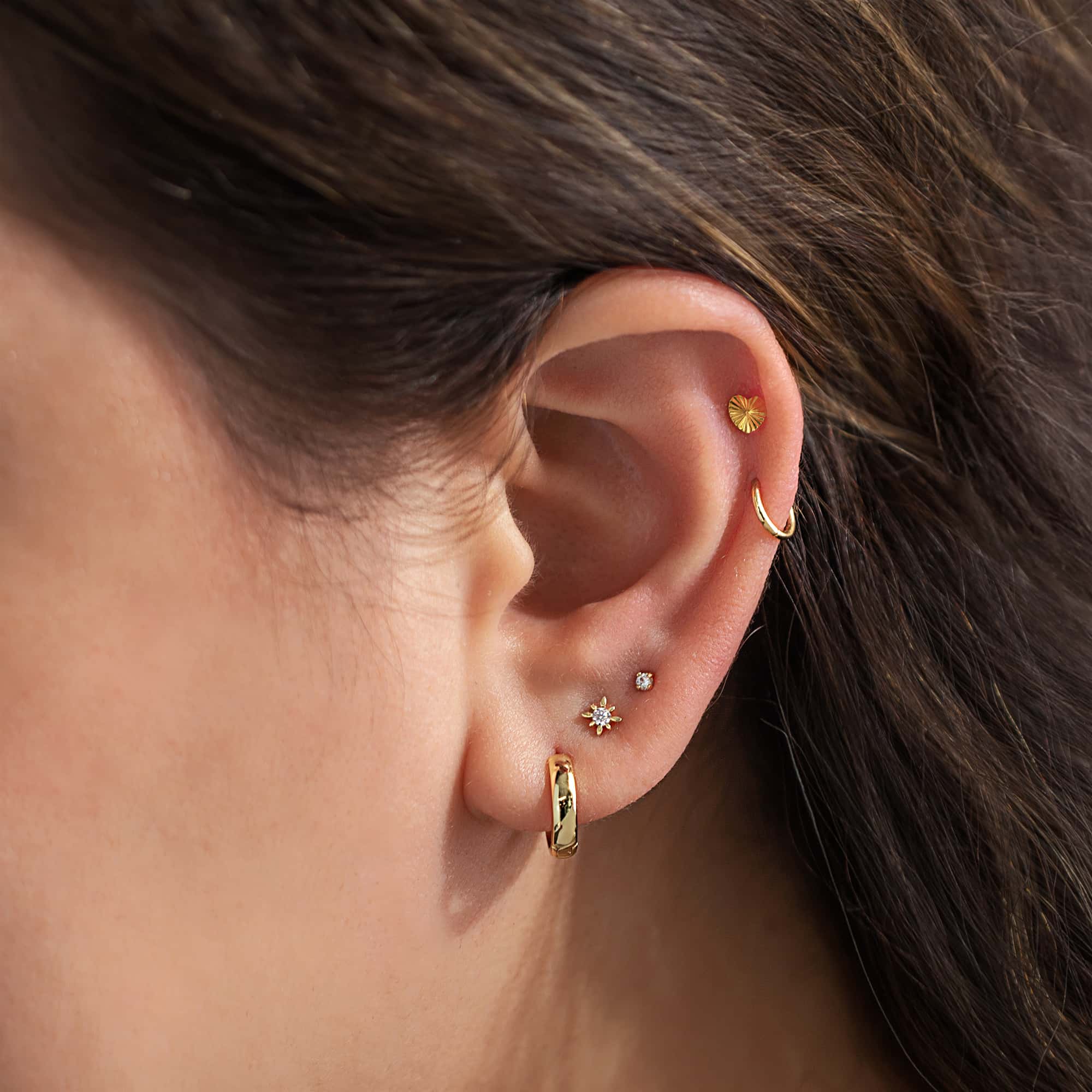 Gold ear stack on a model with a small huggie hoop, starburst stud and clear-stone studs across several piercings