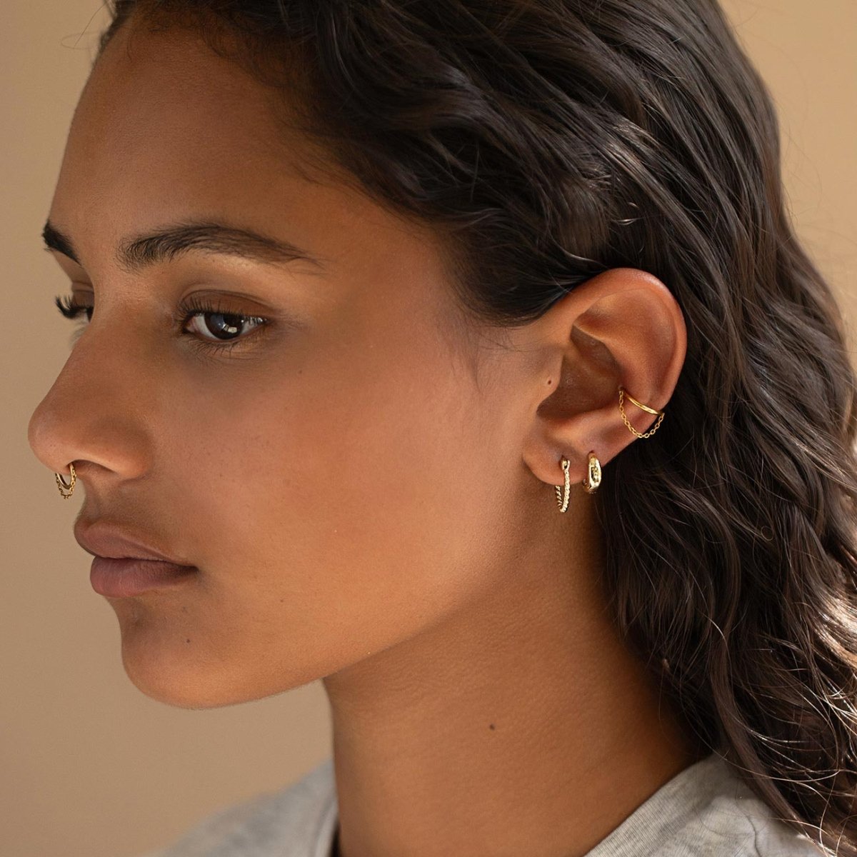 Gold hoops, chained ear cuff and nose ring styled in an ear stack on a model