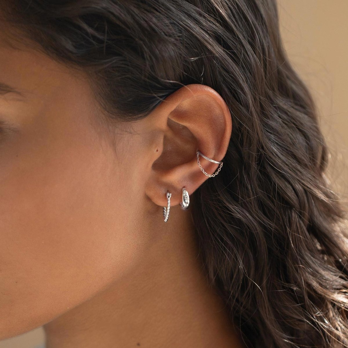 Silver twisted hoops and a chained ear cuff styled in an ear stack on a model