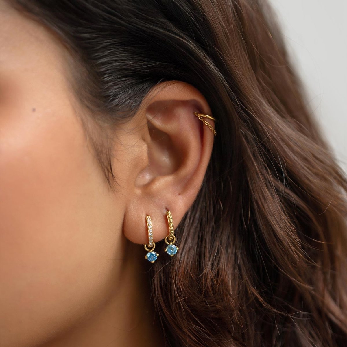Gold vermeil pavé huggie hoops with dangling blue zircon charms, shown on a model's ear
