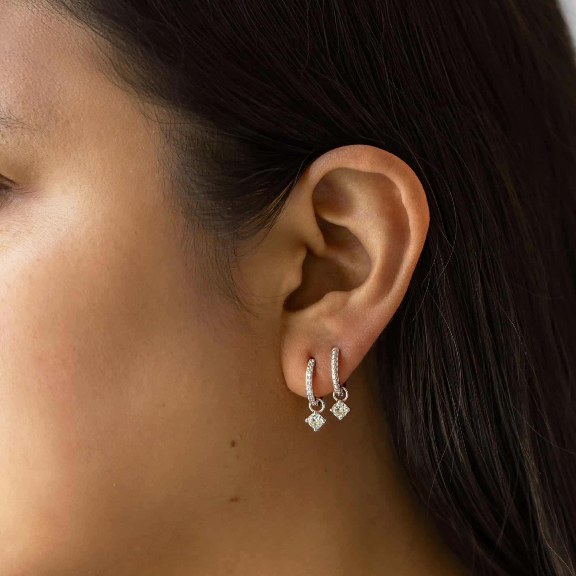 Sterling silver pavé huggie hoops with dangling white zirconia charms, shown on a model's ear