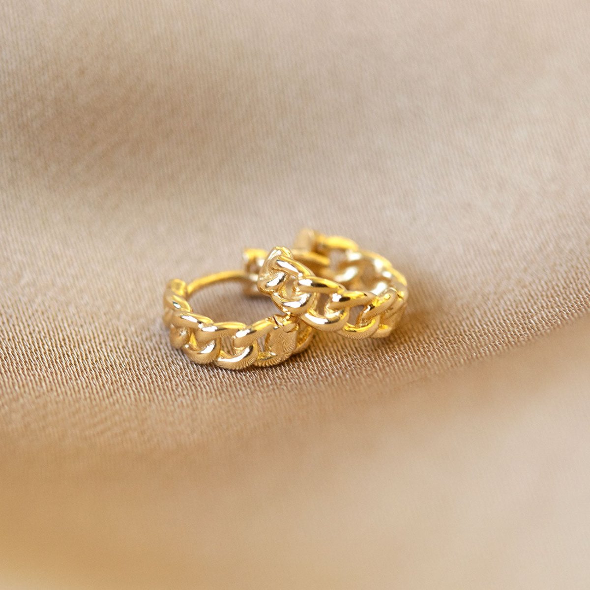 Gold vermeil curb chain link huggie hoops, close-up detail on cream fabric