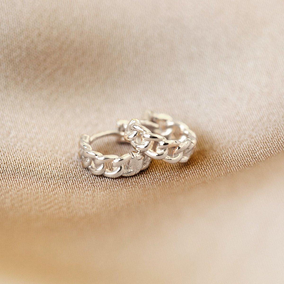 Sterling silver curb chain link huggie hoops, close-up detail on cream fabric