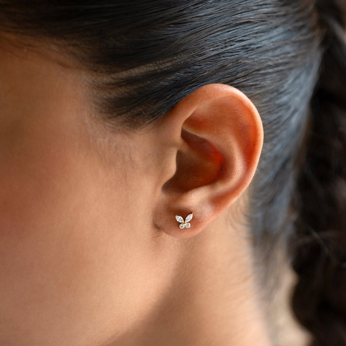 Gold Titanium butterfly-shaped flat back stud earrings shown on a model's ear.