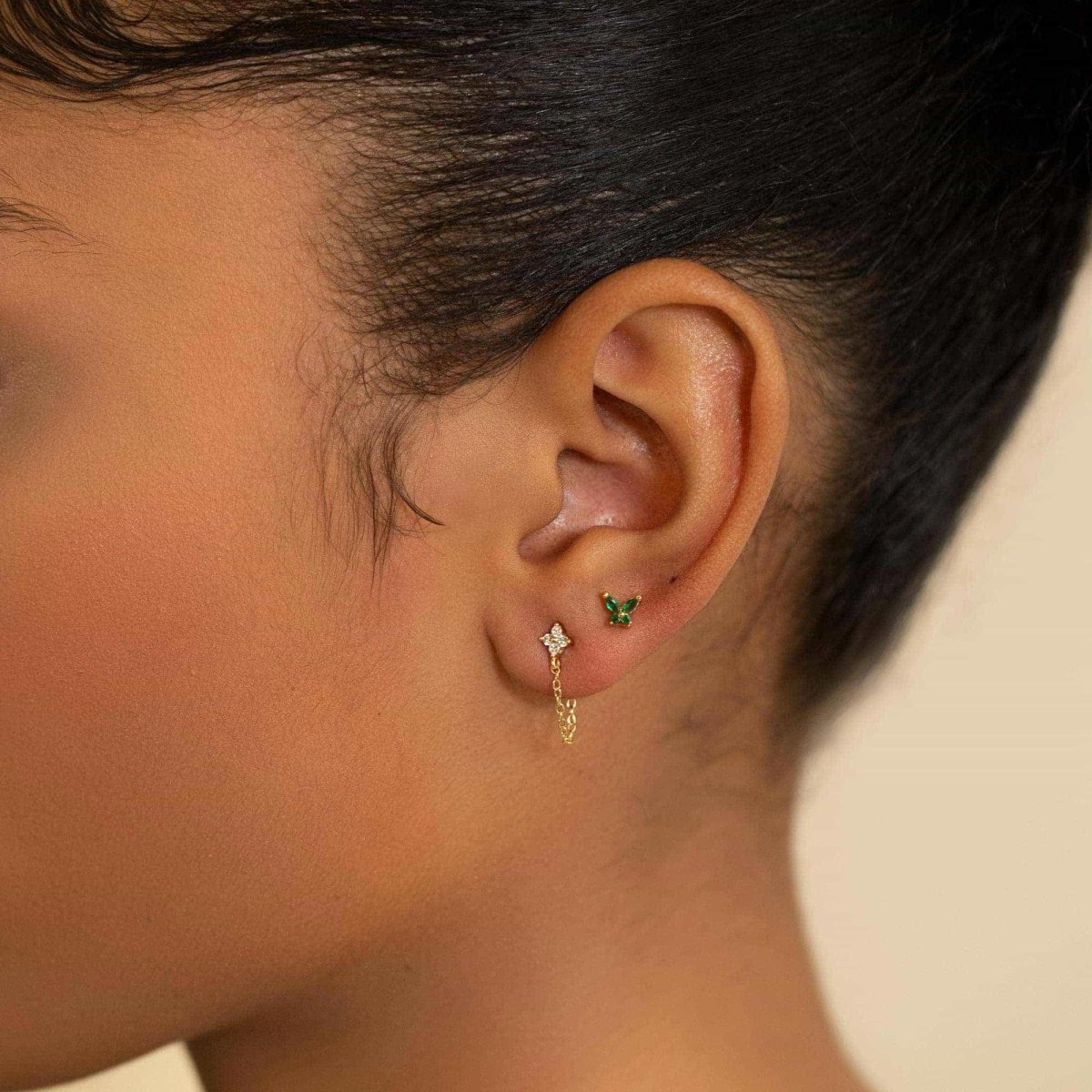 Gold vermeil emerald butterfly and clear flower chain studs shown on a model's lobe and ear