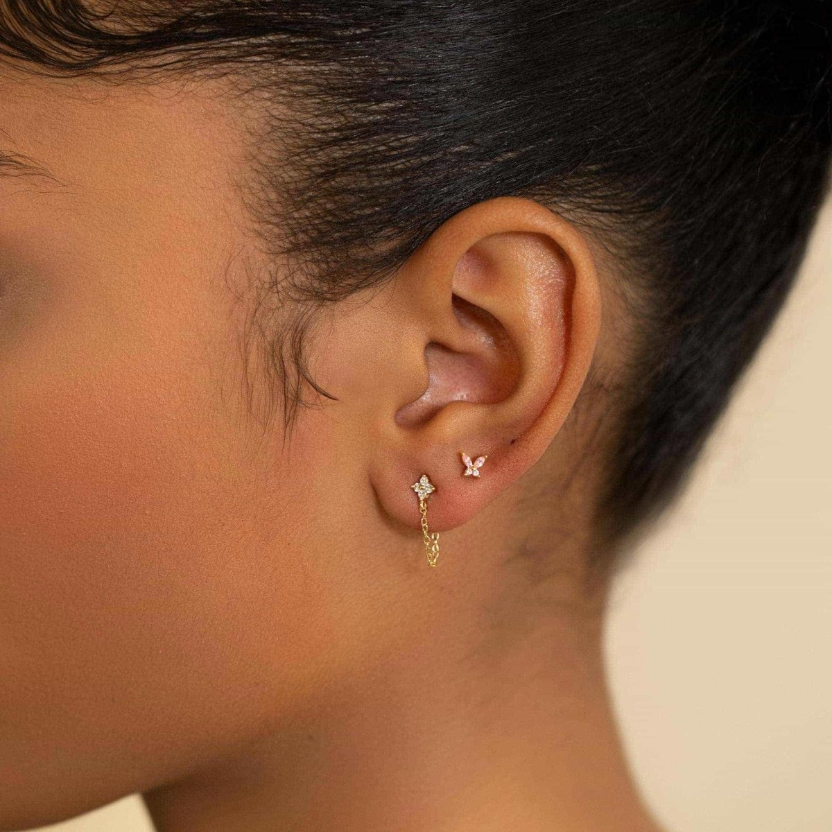 Gold vermeil pink sapphire butterfly and clear flower chain studs shown on a model's ear