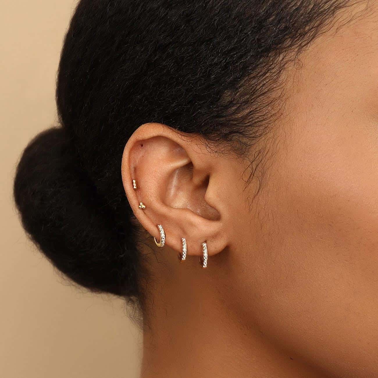 Gold titanium trinity-bead flat back studs styled across a model's lobe piercings
