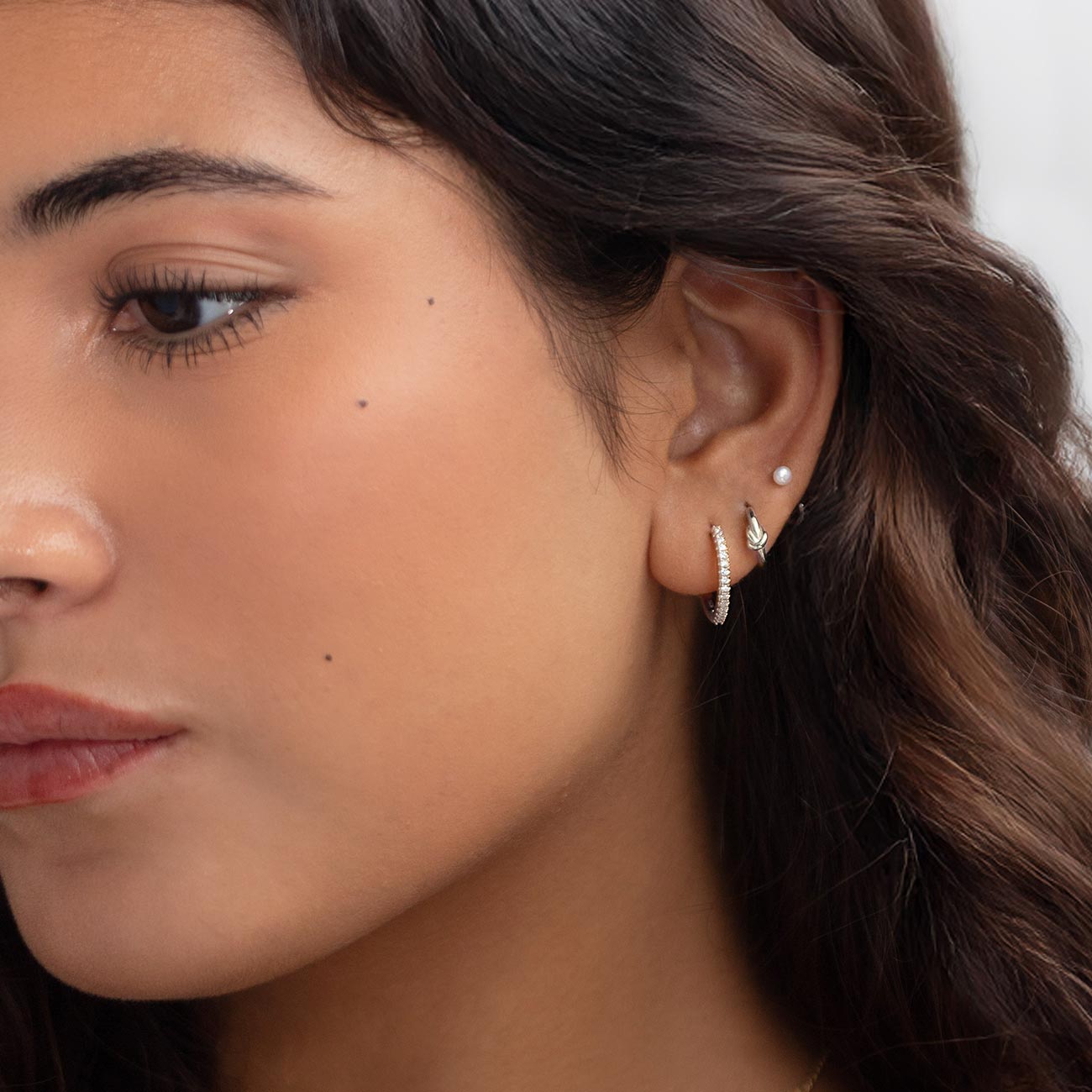 Silver pavé hoop, pearl stud and leaf earring shown in an ear stack on a model