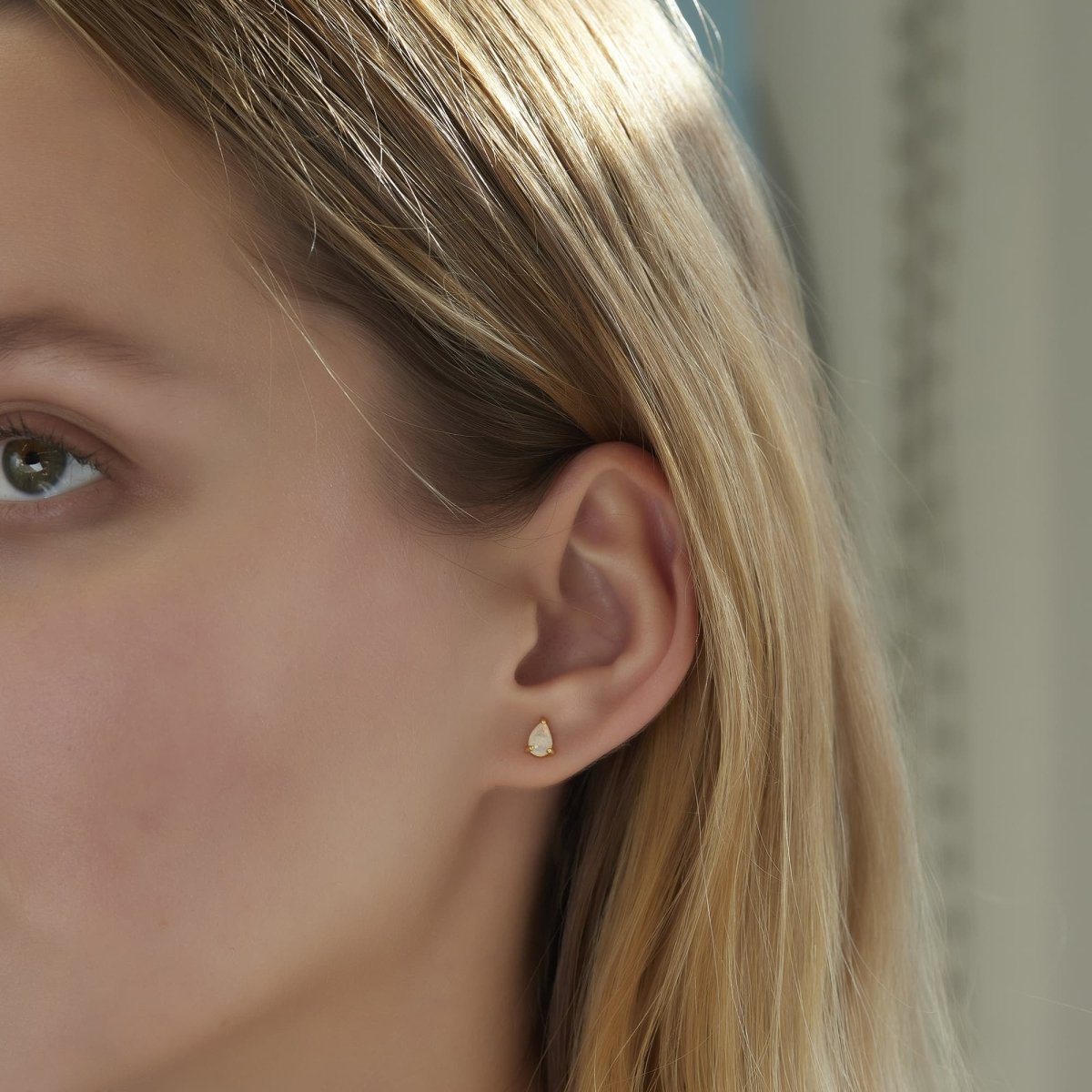 Gold vermeil pear-shaped white opal stud earrings styled with opal huggies on a model's lobe