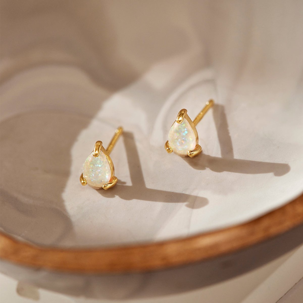 Gold vermeil pear-shaped white opal stud earrings, close-up detail on a cream dish