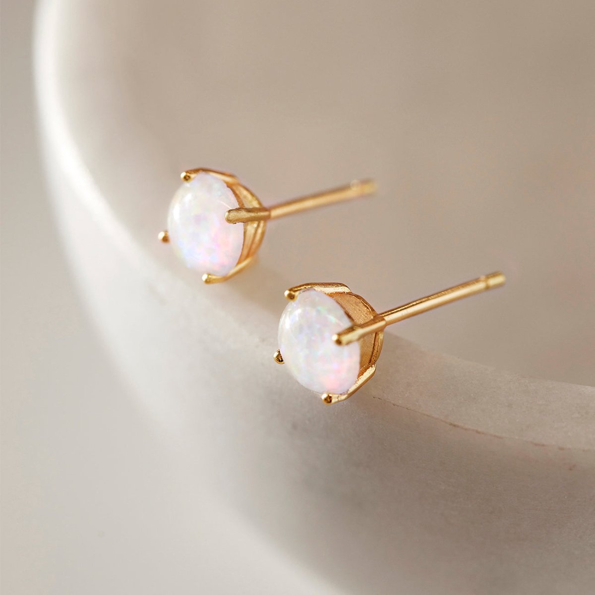 Gold vermeil solitaire studs with round white opal stones, close-up on a cream dish