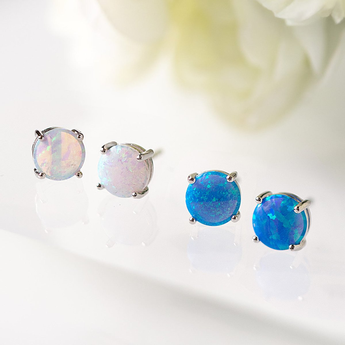 Sterling silver solitaire opal stud earrings with white and blue opal stones, on a white surface