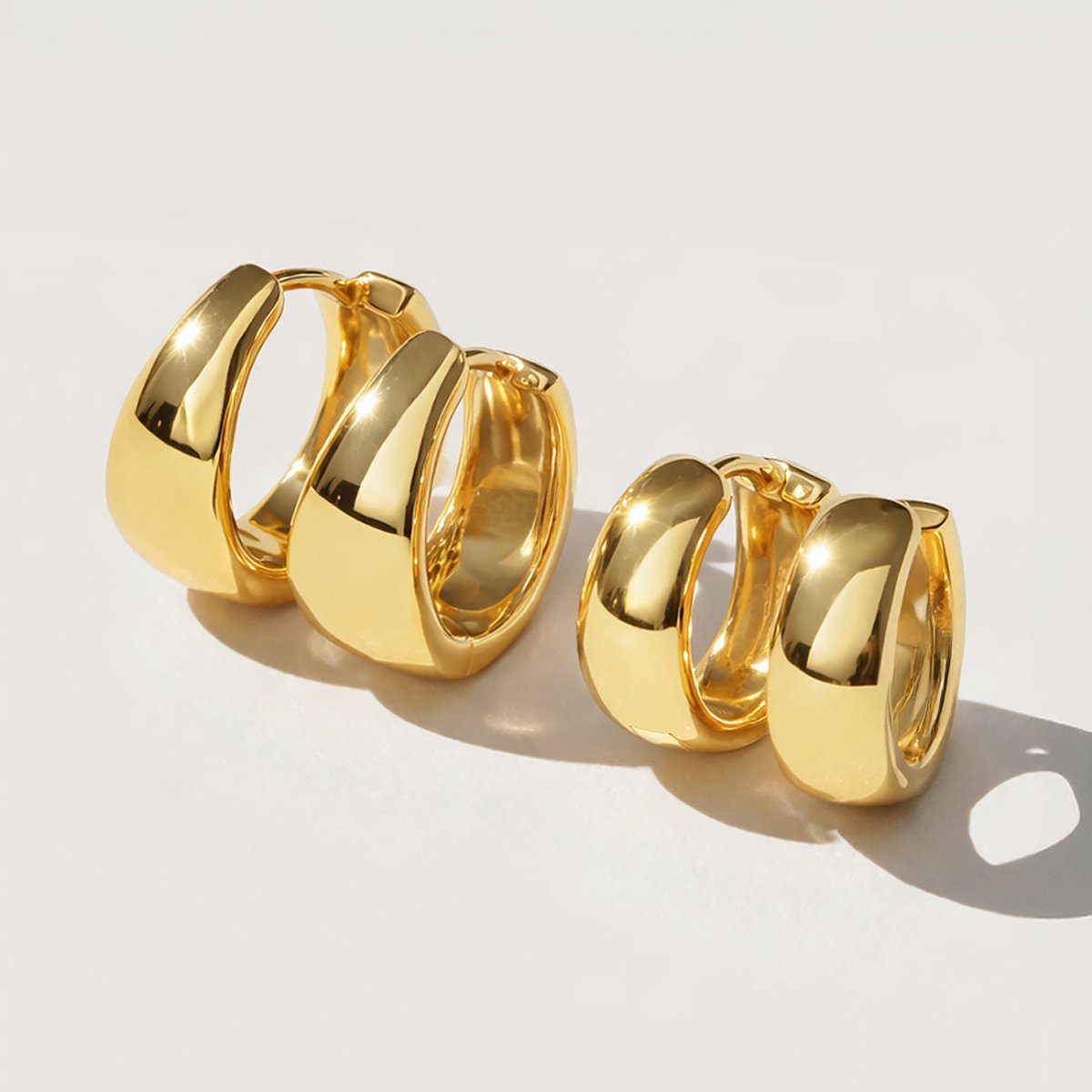 Two pairs of gold chunky dome huggie hoops shown in two sizes, on a cream background