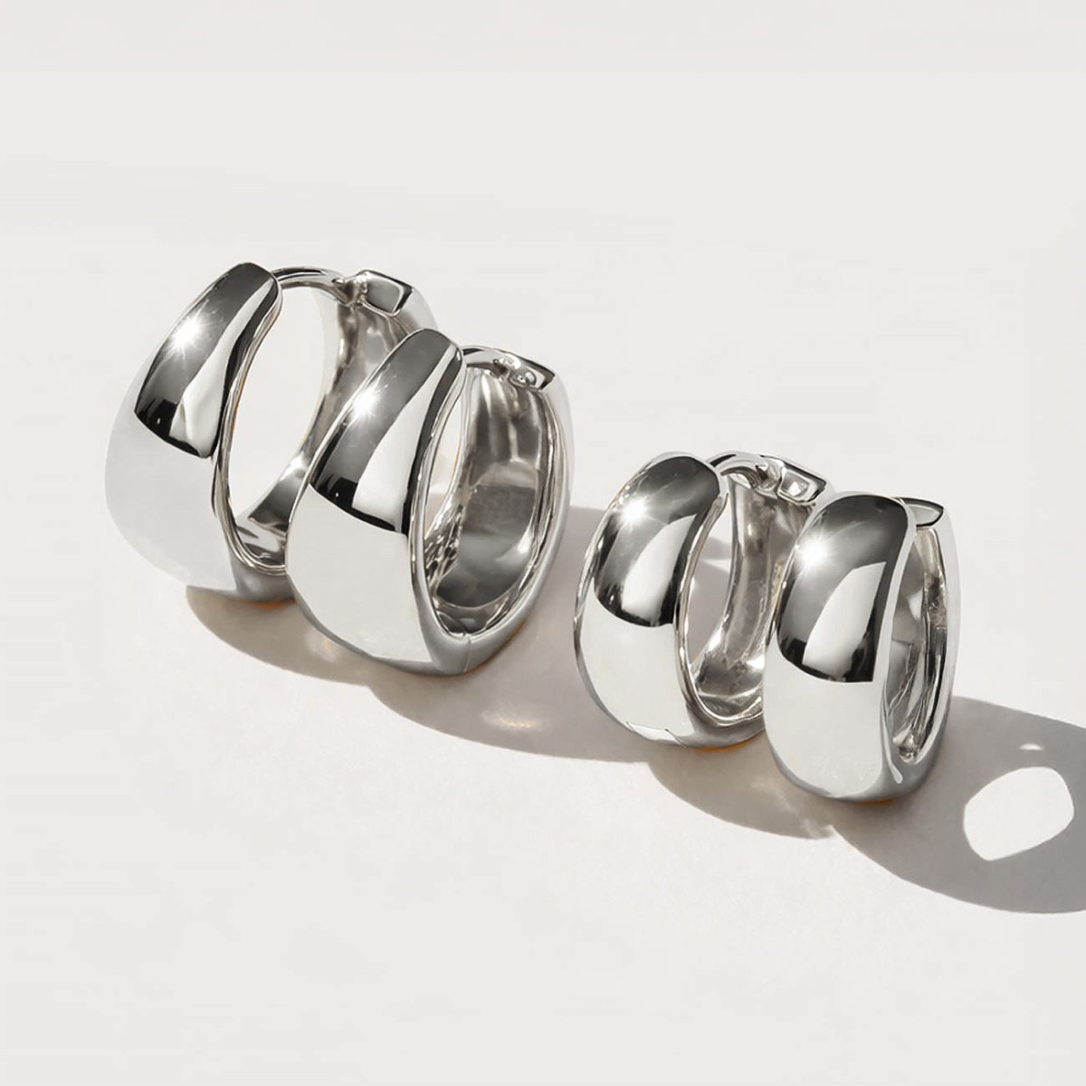 Two pairs of silver chunky dome huggie hoops shown in two sizes, on a white background