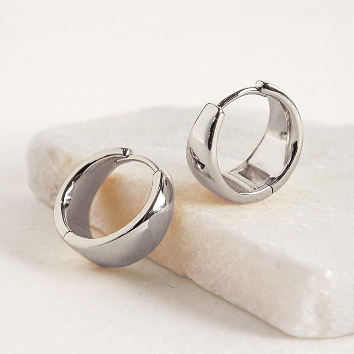 Sterling silver bold teardrop small huggie hoops, shown in two sizes on white marble