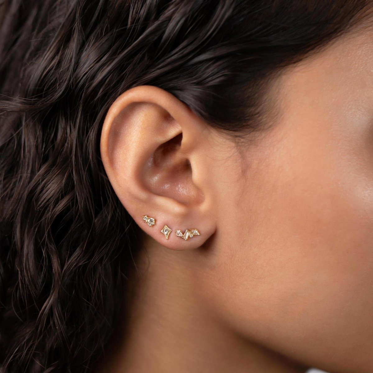 Gold vermeil cluster studs with white zirconia stones in a row along a model's lobe