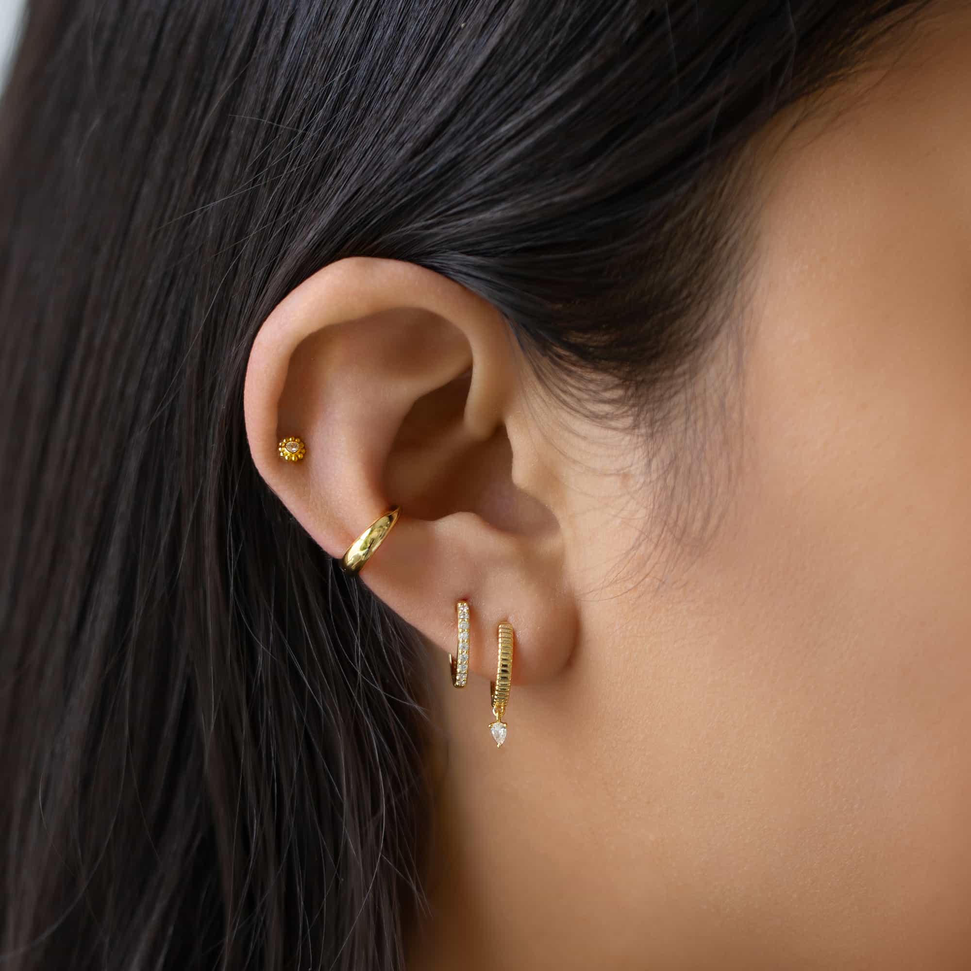 Gold vermeil beaded halo flat back stud shown on a model's lobe with hoops and an ear cuff