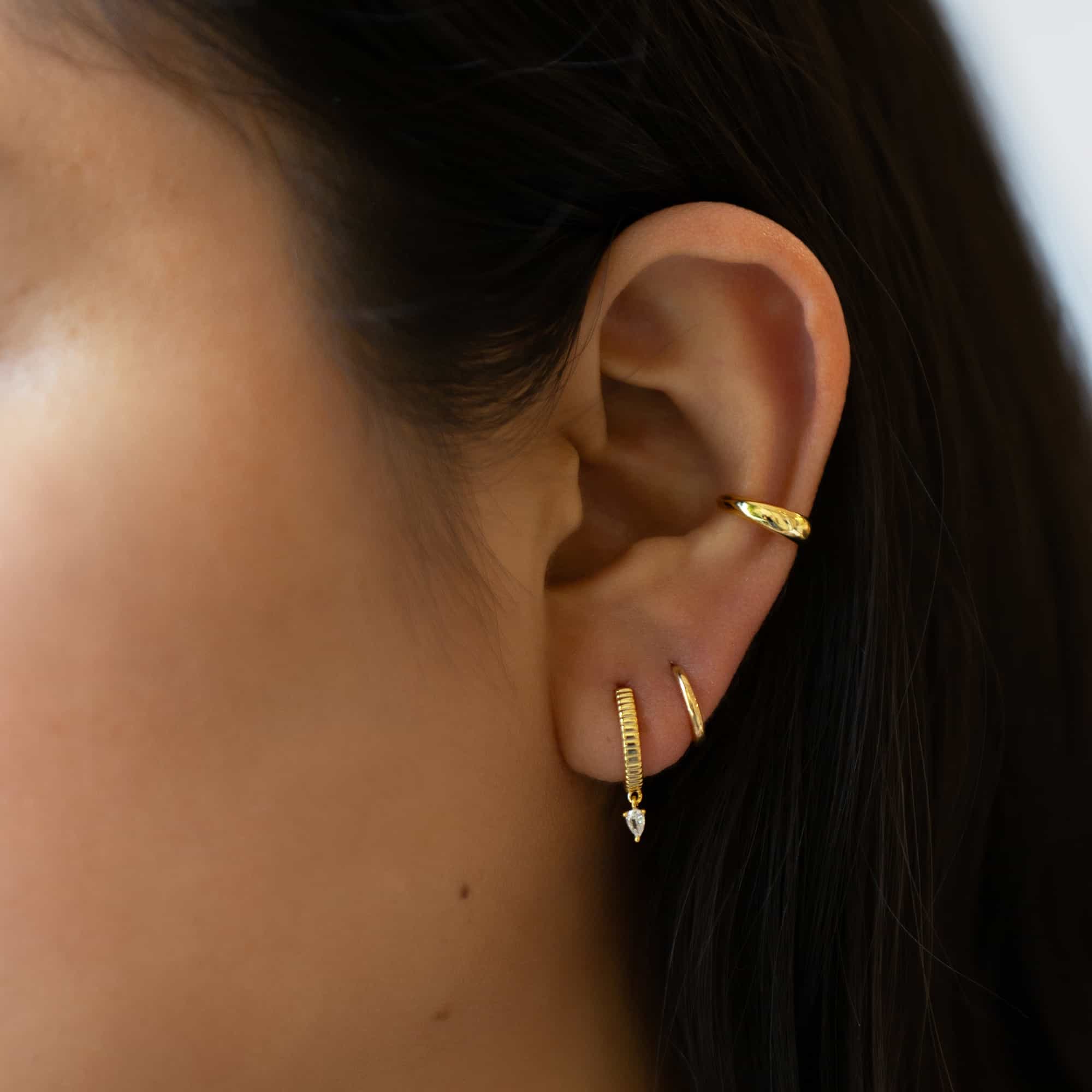 Gold vermeil ridged huggie with a dangling pear white zirconia, shown on a model's lobe