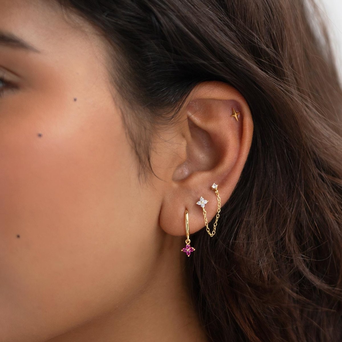 Gold clear-stone chain stud and pink-stone charm huggie shown in a model's ear stack