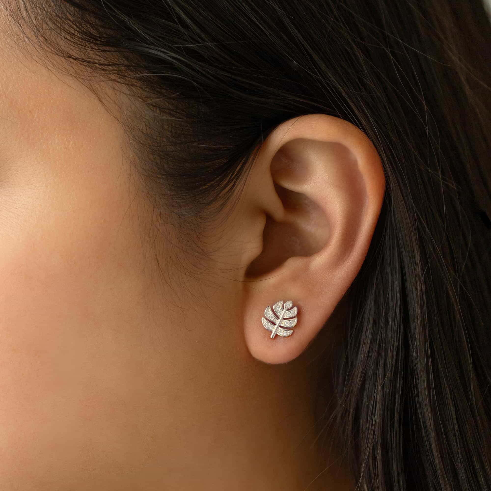 Sterling silver pavé monstera leaf stud with clear stones, shown on a model's lobe