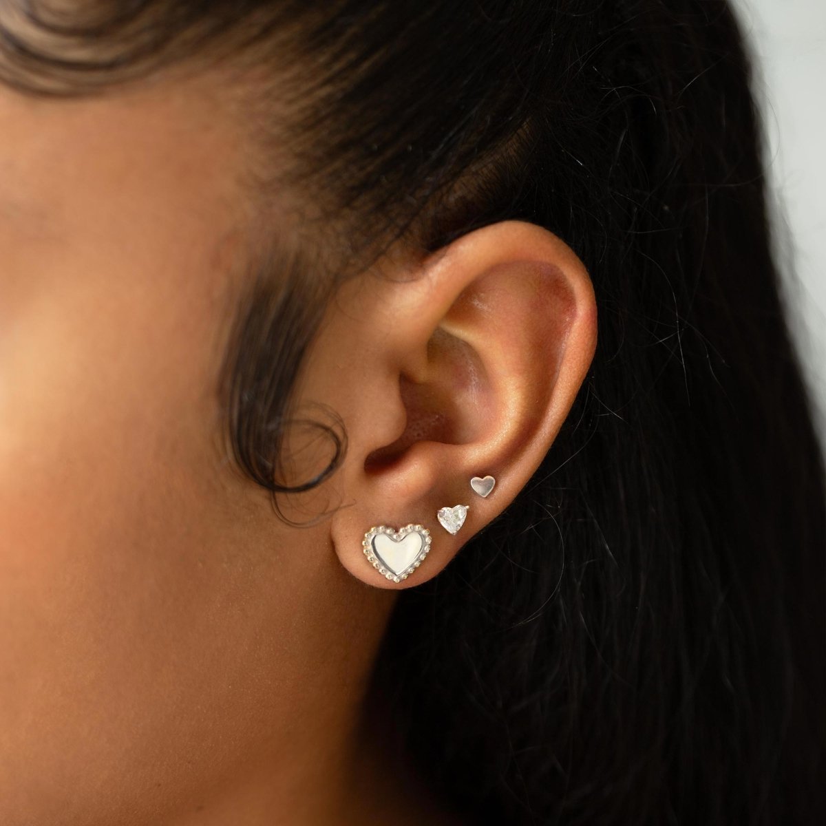 Sterling silver heart stud with a clear white zirconia stone shown on a model's lobe in an ear stack